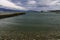 Pier on the sea beach and the lighthouse on the background of mountains and overcast sky.