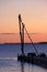 Pier before sunrise with birds sitting on a small crane silhouetted against the morning sky