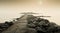 Pier surrounded by stones going through the calm sea with the sunny sky in the background