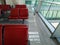 A pigeon walks across the floor past rows of red chairs in a room with large panoramic windows. Bird in empty waiting room of
