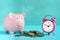 Piggy bank on a blue background. Near a pile of coins and a pink alarm clock. The symbol is the accumulation and