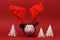 Piggy bank with reindeer horn and jingle bells standing on red background with three white origami trees Christmas background