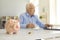 Piggy bank standing on desk with blurred retired man using laptop and doing accounting in background