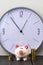 Piggy bank and tower coins on background of clock. Copy space.