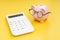 Piggy bank wearing glasses looking at calculator on yellow background using as budget, tax cost and expense calculation or money