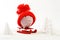 Piggy box with red hat with pompom standing on red sled on snow and around are snowbound trees