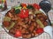 Pilaf with pork is laid out on a metal dish. The food is decorated with tomatoes, herbs, pepper