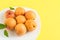 Pile of apricots in a white plate on a flat yellow background