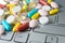 Pile of assorted medicine pills and capsules on gray keyboard, macro pharmaceutical background.