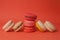 Pile of colorful macaroons stacked up like a tower and macarons on their two sides in red pastel background.