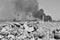 A pile of concrete rubble with protruding rebar on the background of thick black smoke in the sky. Background. Black and white