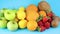 Pile of different fresh organic fruits on blue background. Oranges, apples, kiwi, strawberries, lemons and coconut