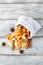 A pile of dried slices of apples and spices pills out of a white pouch on wooden background. Dried fruit chips