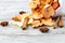 A pile of dried slices of apples and spices pills out of a white pouch on wooden background. Dried fruit chips