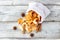 A pile of dried slices of apples and spices pills out of a white pouch on wooden background. Dried fruit chips