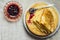 Pile of folded golden crepes on white plate, spilled black currant jam in crystal rosette, spoon, linen cloth