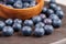 A pile of fresh blue bilberry on a brown board with wooden bowl. Ripe blueberries