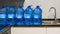 Pile of gallons of water beside a sink inside a white-tiled kitchen