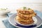 pile of golden crisp vegetables rosti from cauliflower and parmesan cheese with a creamy dip and parsley garnish on a blue napkin