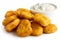 Pile of golden deep-fried battered chicken nuggets with bowl of