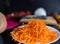 Pile of grated carrot on white plate with blurry vegetables as background