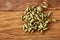 Pile of green cardamon seeds on rustic wooden background close-up, top view, selective focus.