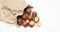 Pile macadamia nuts open kernels and shells in burlap bag on white background, top view