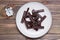 A pile of molded pieces of chocolate on a plate and an alarm clock on a wooden table. The concept of eating sweet time