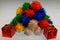 A pile of multi coloured pom poms with a wrapped present in the front