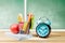 Pile of notebooks with apple and pencils in basket container with green stapler and alarm clock on the wooden table