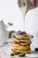 Pile of pancakes with blueberry on the top, maple leaf is pouring on it by a woman`s hand.