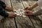 Pile of puzzle pieces lying on wooden desk with four hands reach