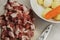 Pile of raw fresh sliced meat on a white plastic cutting board with knife and white bowl filled with potatoes, onions and carrots