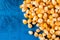 Pile of raw popcorn above blue wooden background with copy space