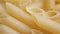 A pile of raw yellow pipe-shaped pasta lies on the surface. Raw pasta feathers in large quantities on the table.