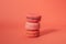 Pile of red-toned macaroons stacked up like a tower in red pastel background.