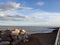 Pile of rocks on the beach under blue cloudy sky seen from walkway on the shore