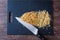 Pile of rough chopped and fine chopped walnuts on a black cutting board, chef knife, on dark wood table