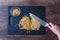 Pile of rough chopped and fine chopped walnuts on a black cutting board, womanâ€™s hand on chef knife, glass bowl.