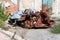 Pile of rusted crumpled sheet metal in front of abandoned cracked factory wall surrounded with rubble and grass