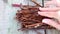 A pile of rusty nails on the wooden surface, which the hand is sorting through.