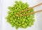 Pile of shelled edamame on a square white plate with chop sticks