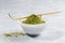 Pile with slide of green matcha tea powder in white bowl with special wooden bamboo spoon on grey textured backdrop.