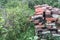 Pile of stacked rows of old, cracked, burnt bricks in an abandoned, unkempt, overgrown garden in summer