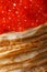 A pile of thin crepes with red caviar macro. vertical