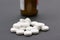 Pile of white pills with brown pill bottle in backgroundll bottle illustrating vitamins or addiction to drugs. Close up landscape