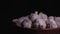 Pile of whole bulbs of garlic in ceramic bowl on table. Harvest of unpeeled vegetables on black background.