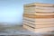 Pile of yellowed old used paperback books on wood desk and light blue background