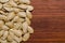 Piled up pumpkin seeds on the left side of the photo on a dark wooden surface.