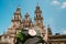 Pilgrim`s backpack with famous pilgrims` mascot and sign seashell with Cross of Saint James at  on the Obradeiro square plaza